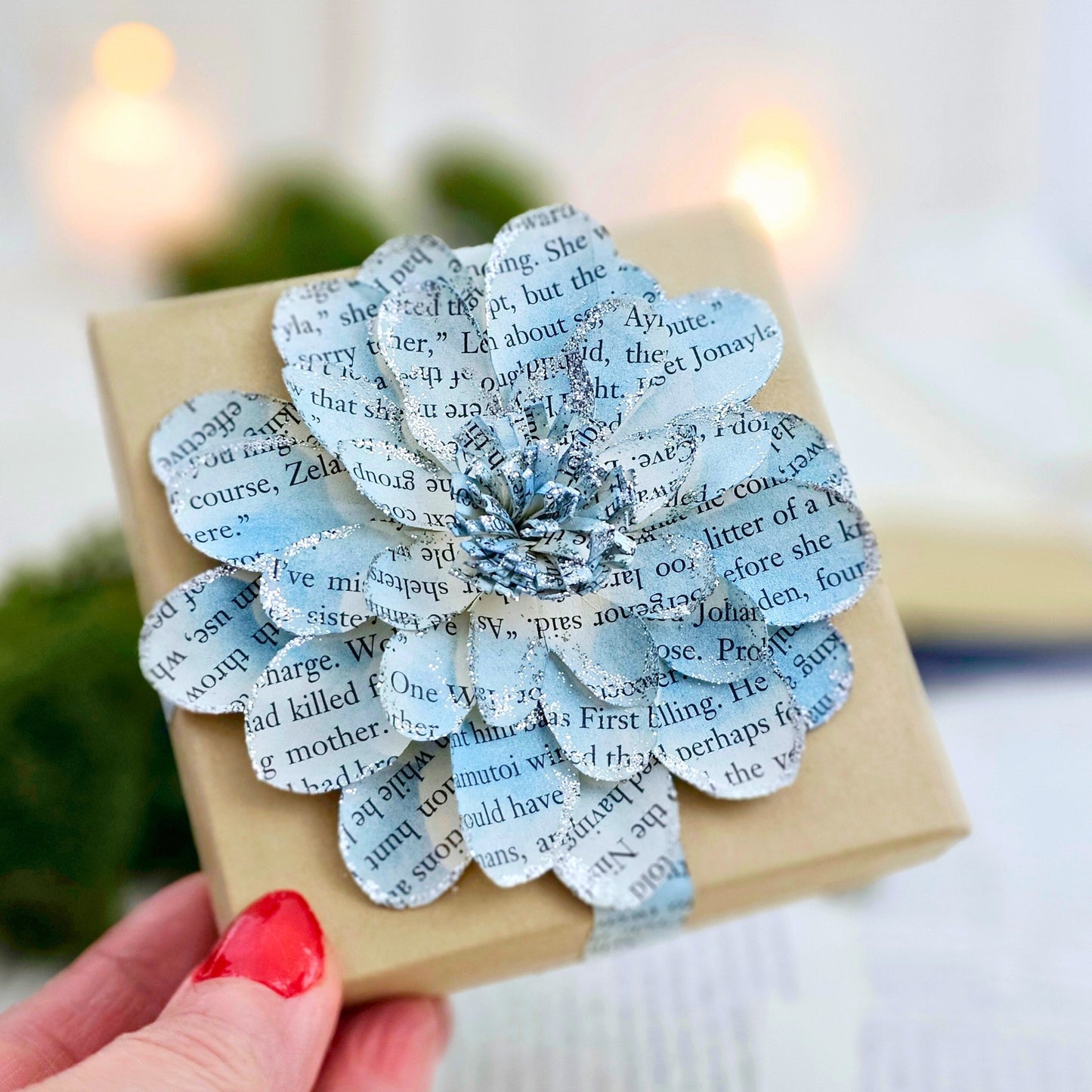 3.5 x 3.5 inch jewelry gift box adorned with a flower made from book pages. It is stained blue and has silver sparkly on the edges.
