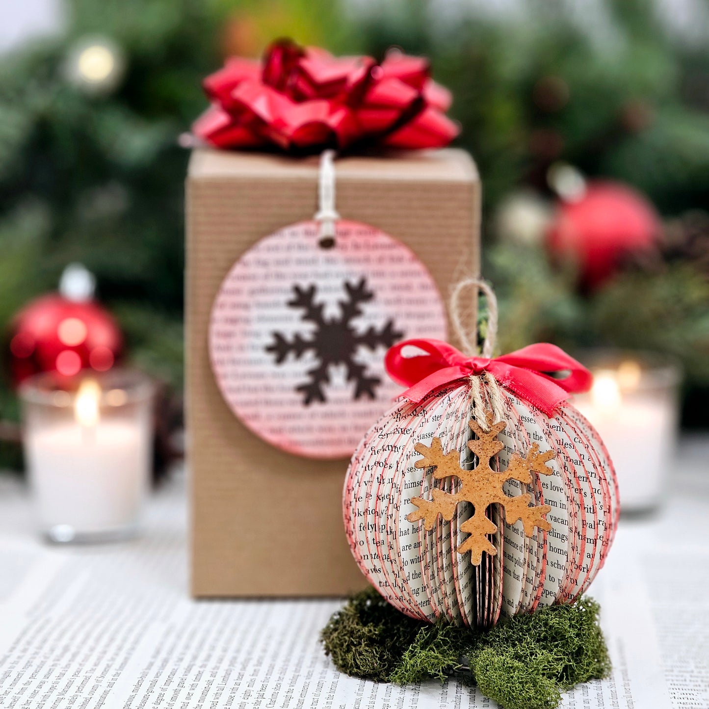 Round ball book page ornament made from book pages. It has a jute string for hanging, a red bow on the top and a rustic metal snowflake on the front. It comes in a gift box with a bow and a gift tag made from a book page.