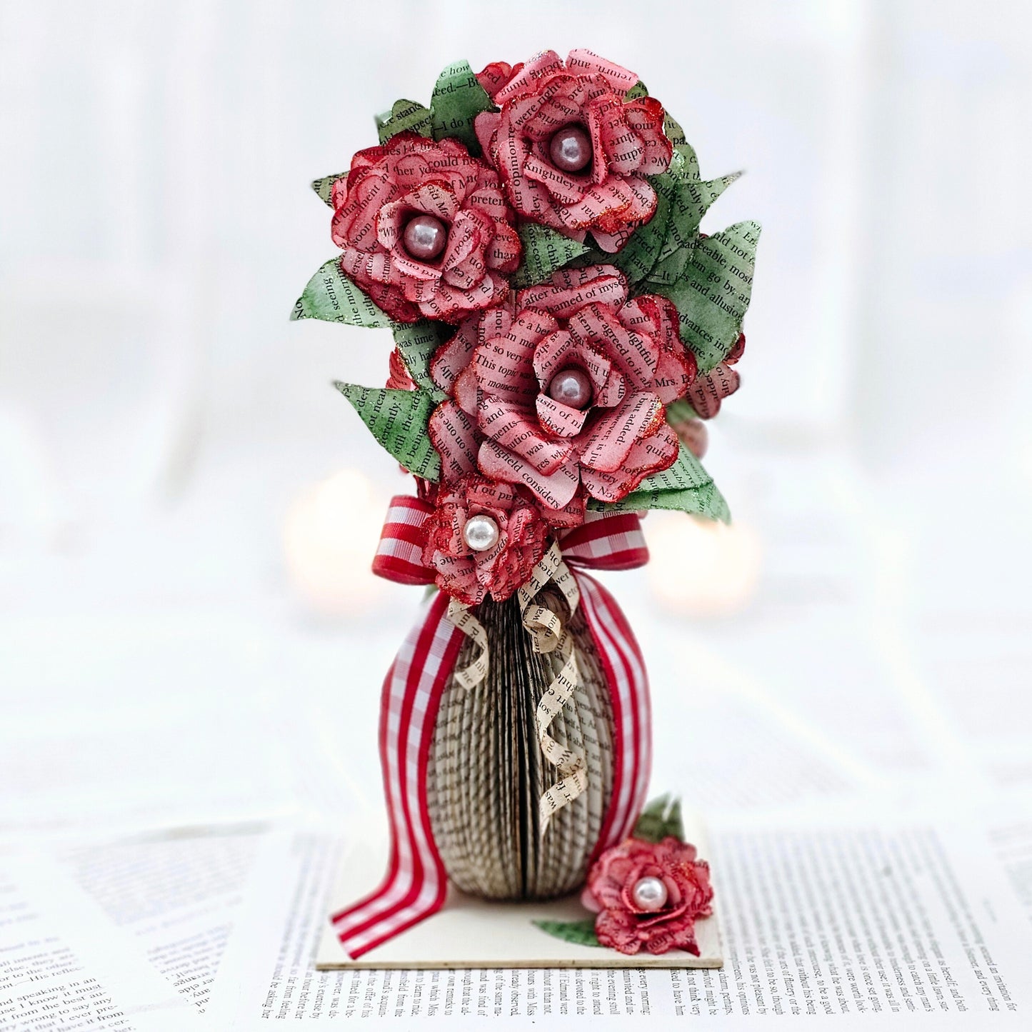 9 inch tall book page flower bouquet, the roses are stained red. The vase is made from book pages . The entire piece sits on a base made from the book cover.