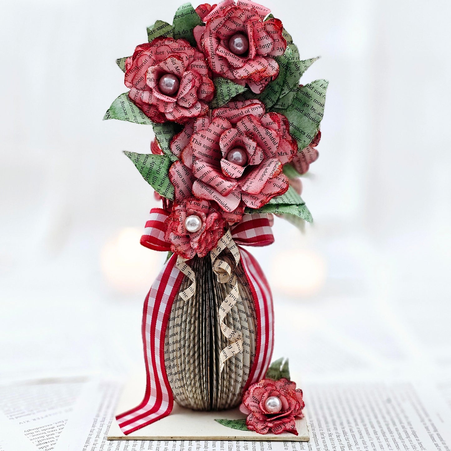 9 inch tall book page flower bouquet, the roses are stained red. The vase is made from book pages . The entire piece sits on a base made from the book cover.