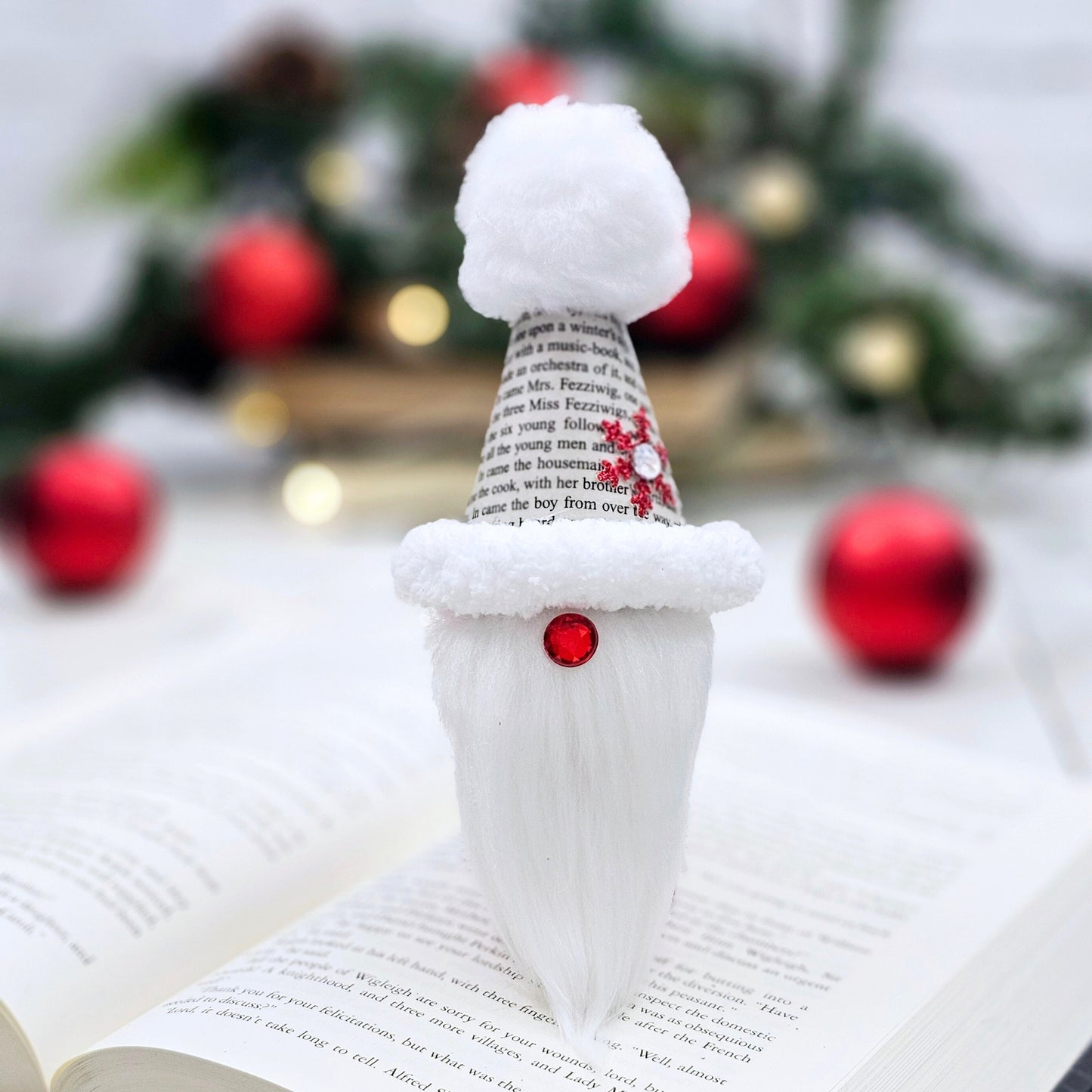 Book Page Gnome Christmast onrament. Artisan made. The body is made of fabric. The hat is made from book pages taken from A Christmas Carol. The hat is lined with fluffy trim and has a white pom on top. The gnome nose is a red acrylic gem .