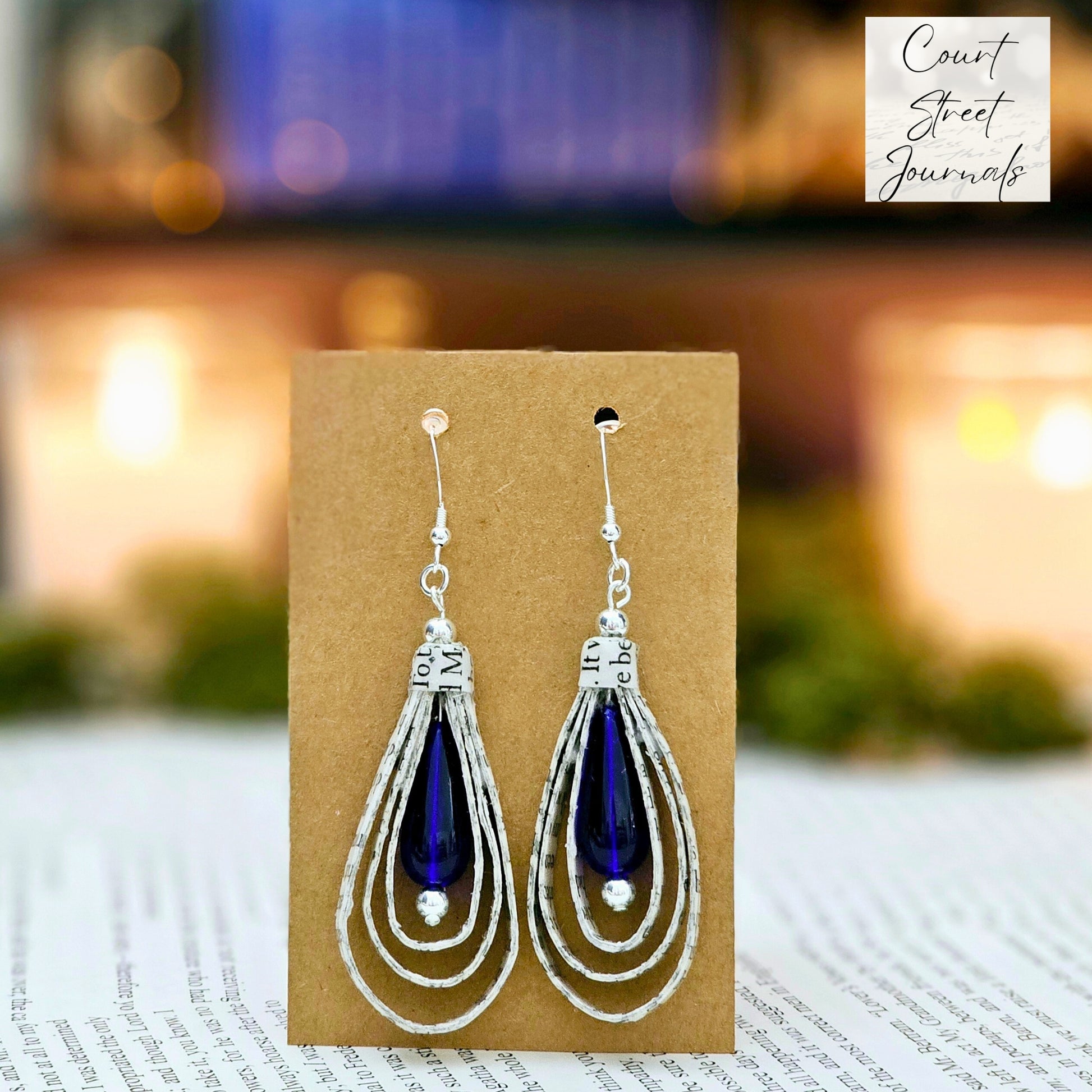 Tear Drop dangle earrings made from upcycled book pages with a blue czech glass tear drop bead accent.  earring is 2.5 inches long.  Sterling silver ear wire.  the earring card states which book the earrings were made from.