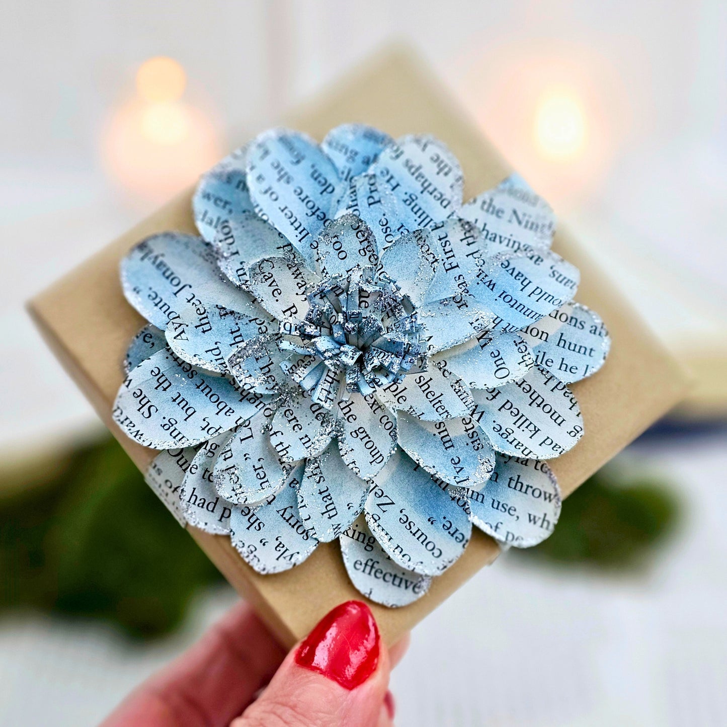 3.5 x 3.5 inch jewelry gift box adorned with a flower made from book pages. It is stained blue and has silver sparkly on the edges.