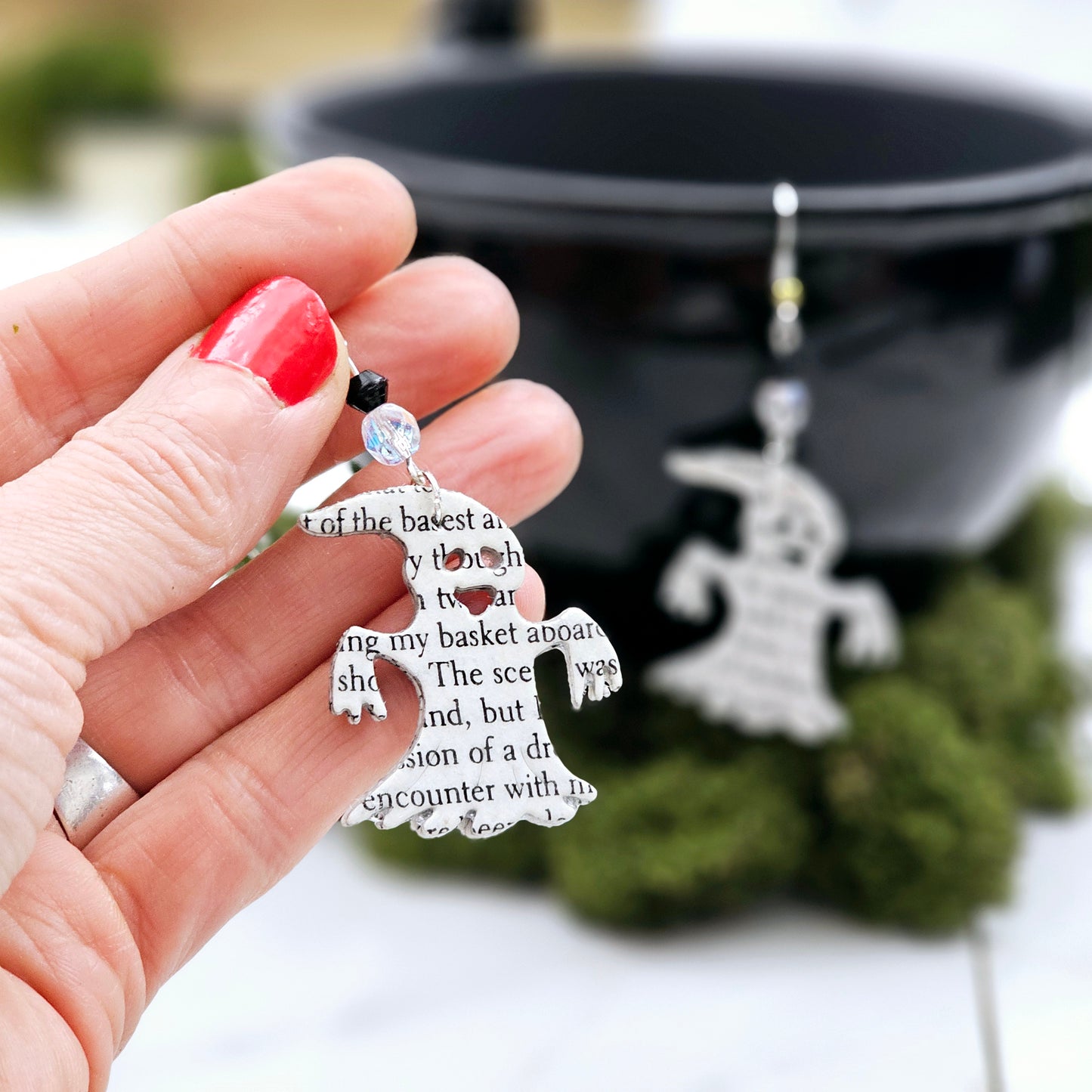 Ghost dangle earrings made from upcycled book pages. Each earring has 2 glass beads above the ghost (one clear one black). The ear wire is silver plated or sterling silver.