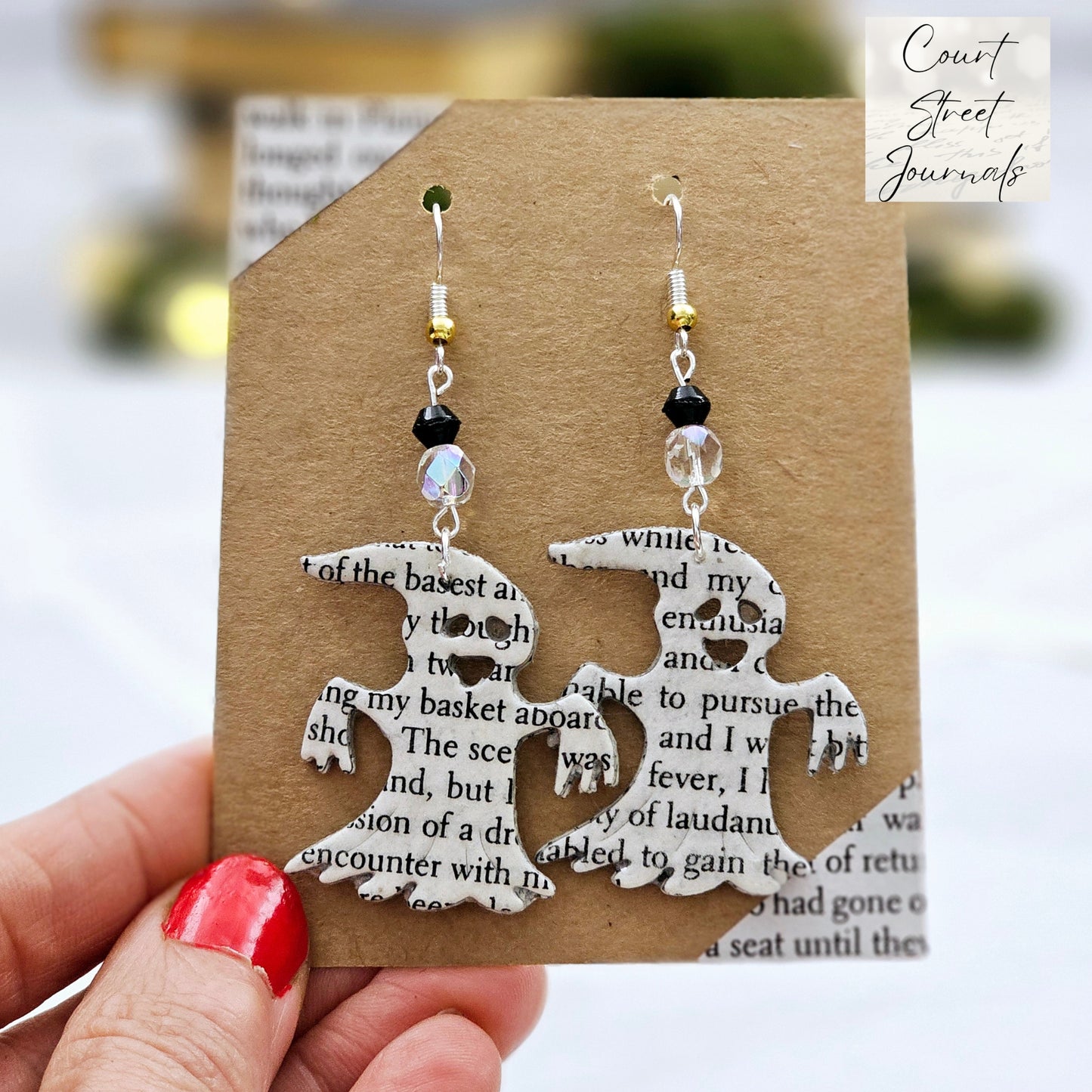 Ghost dangle earrings made from upcycled book pages. Each earring has 2 glass beads above the ghost (one clear one black). The ear wire is silver plated or sterling silver.