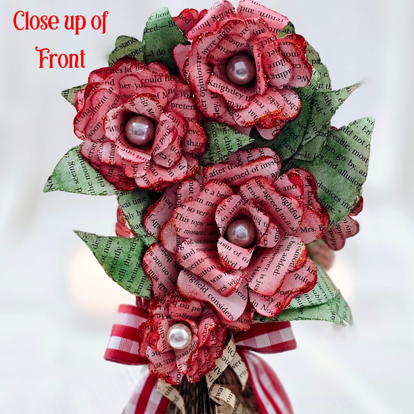 9 inch tall book page flower bouquet, the roses are stained red. The vase is made from book pages . The entire piece sits on a base made from the book cover.