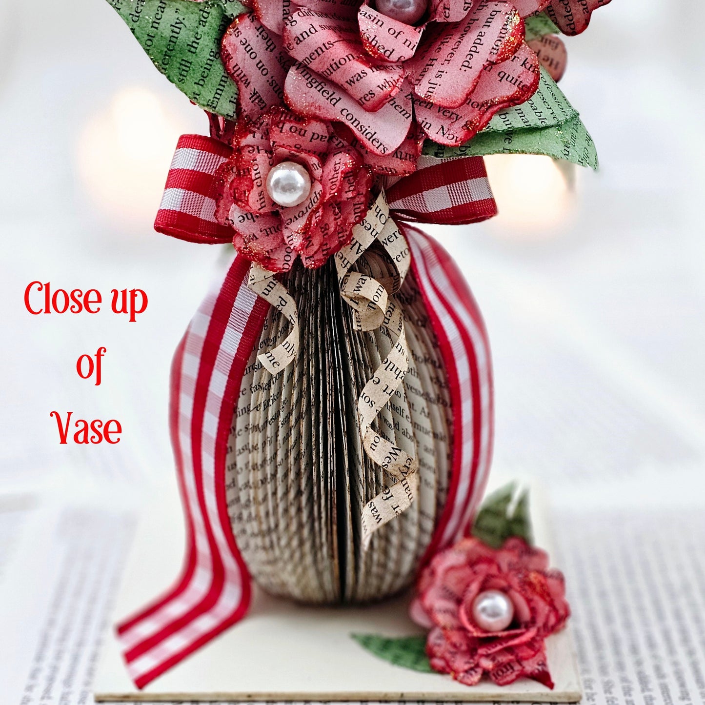 9 inch tall book page flower bouquet, the roses are stained red. The vase is made from book pages . The entire piece sits on a base made from the book cover.