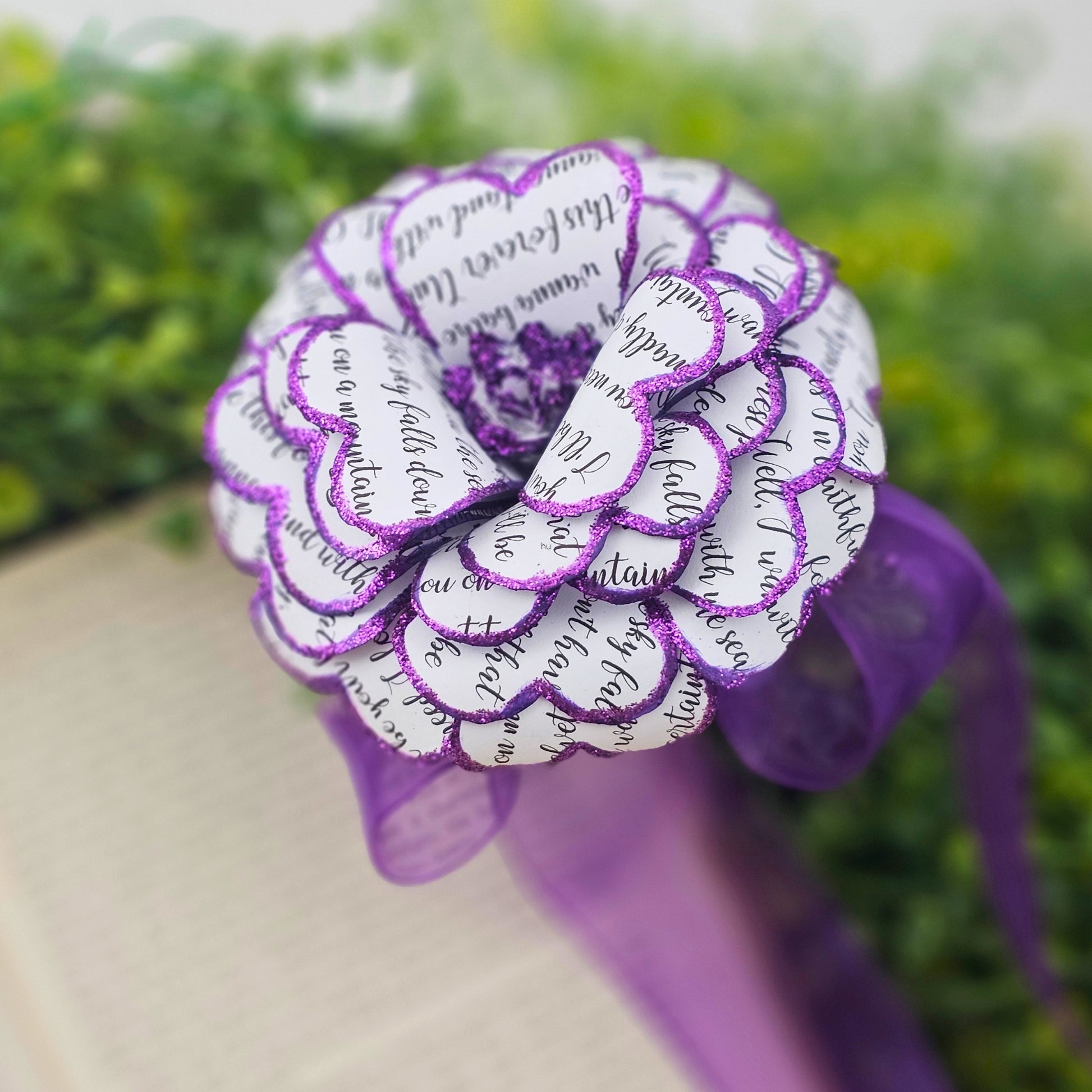 Decorative flower made from paper with purple accents against a blurred green background