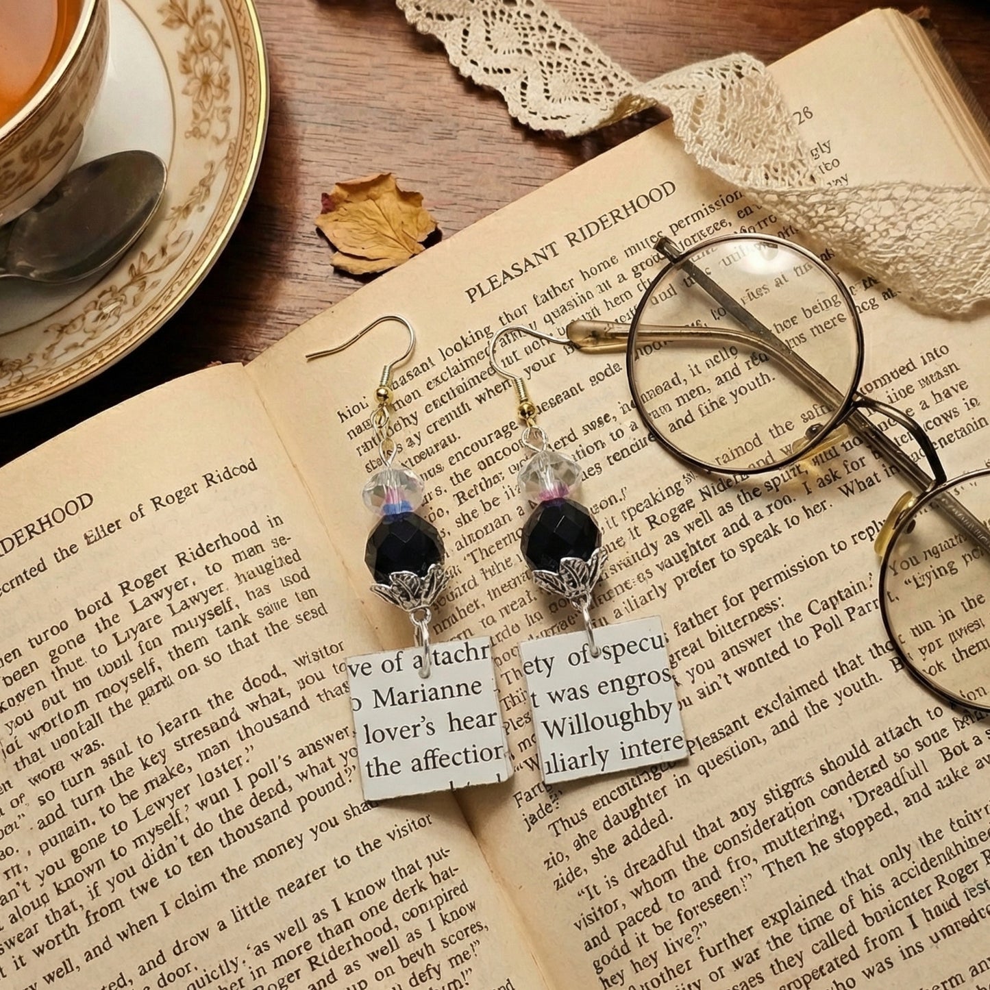 Pair of earrings with text on a book page next to glasses