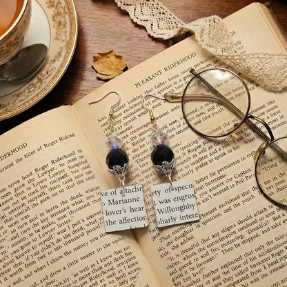 Pair of earrings with text on a book page next to glasses